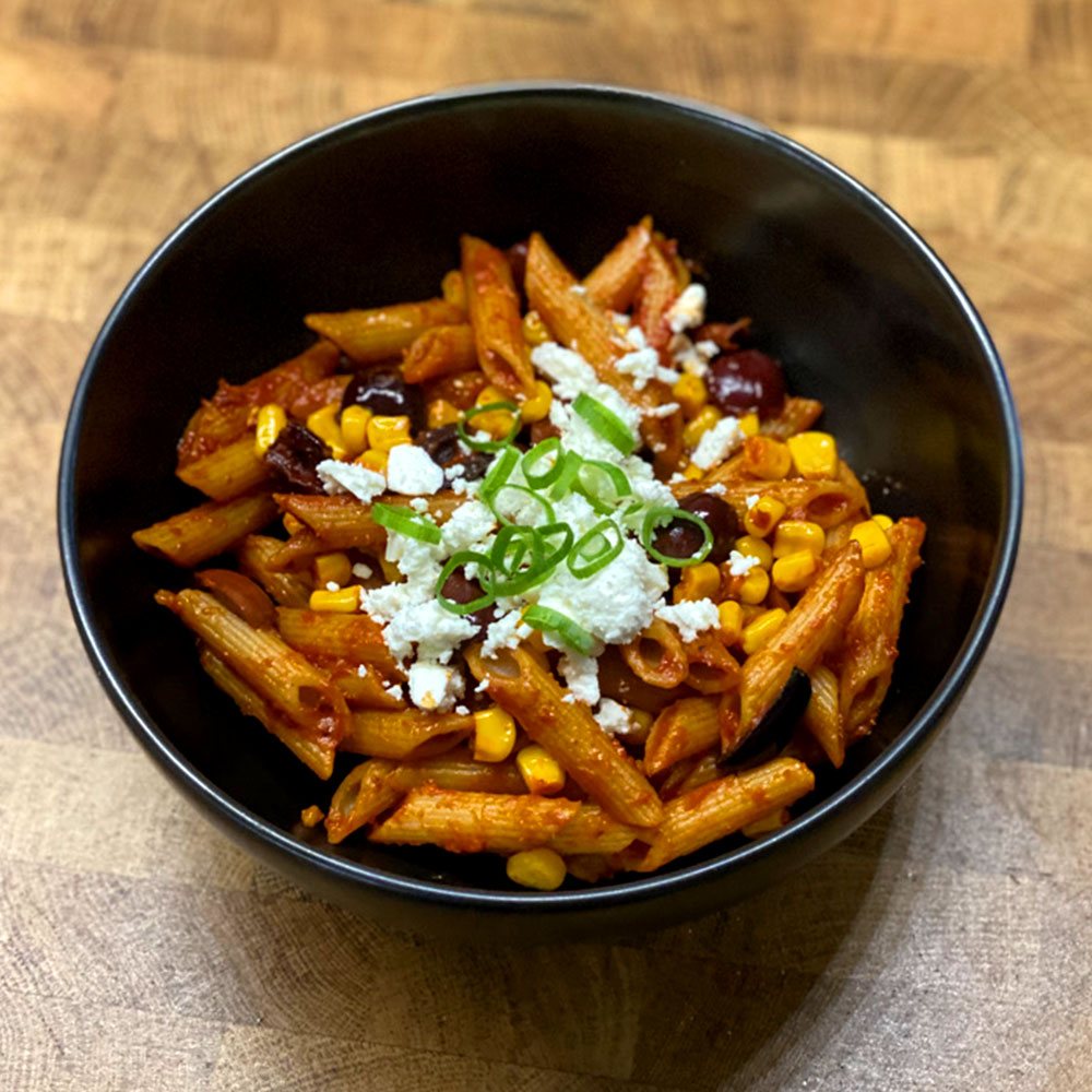 Fried penne arrabiata with corn, olives, feta and spring onion in a black bowl