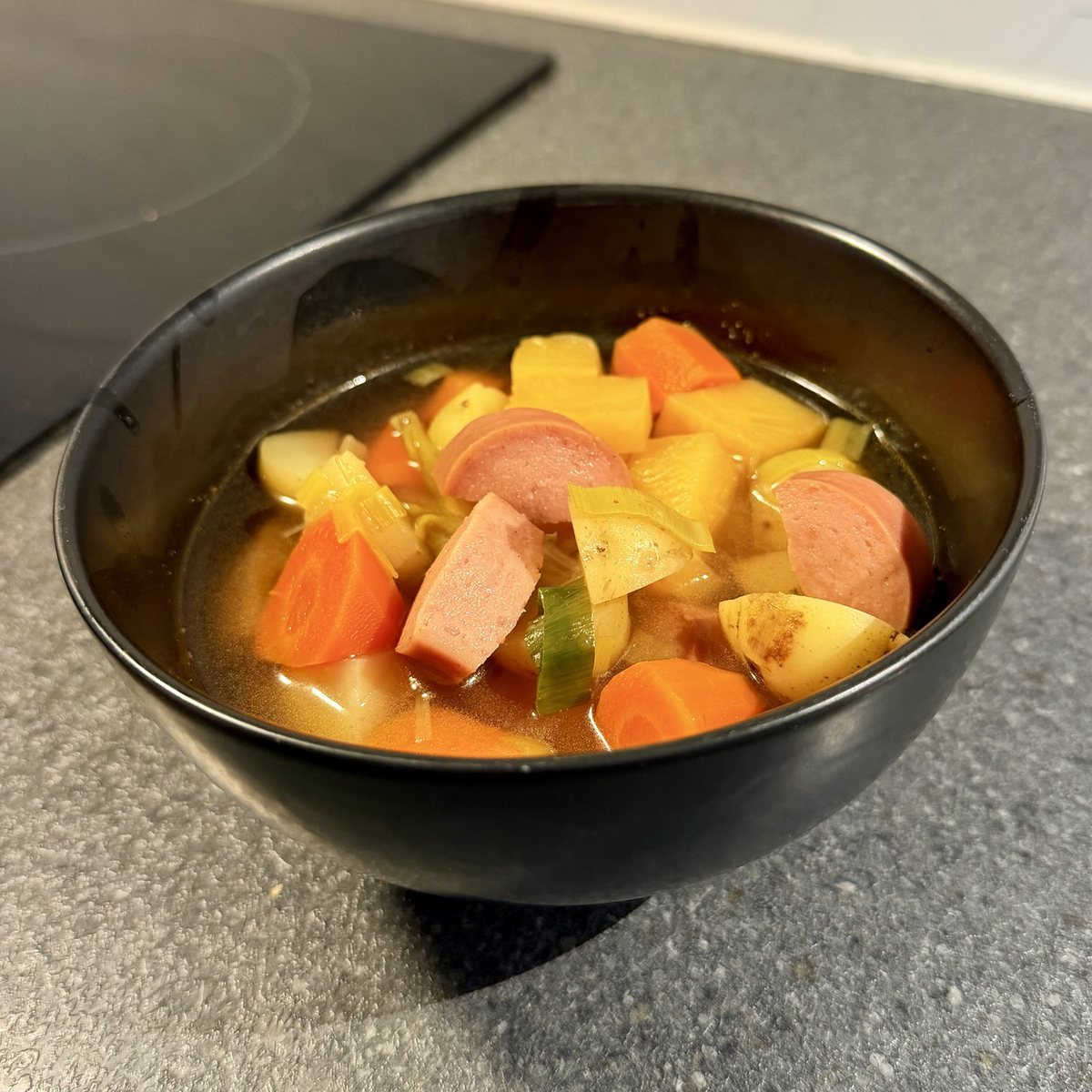 Soup lapskaus with sausage, carrot, potato and leek in a black bowl