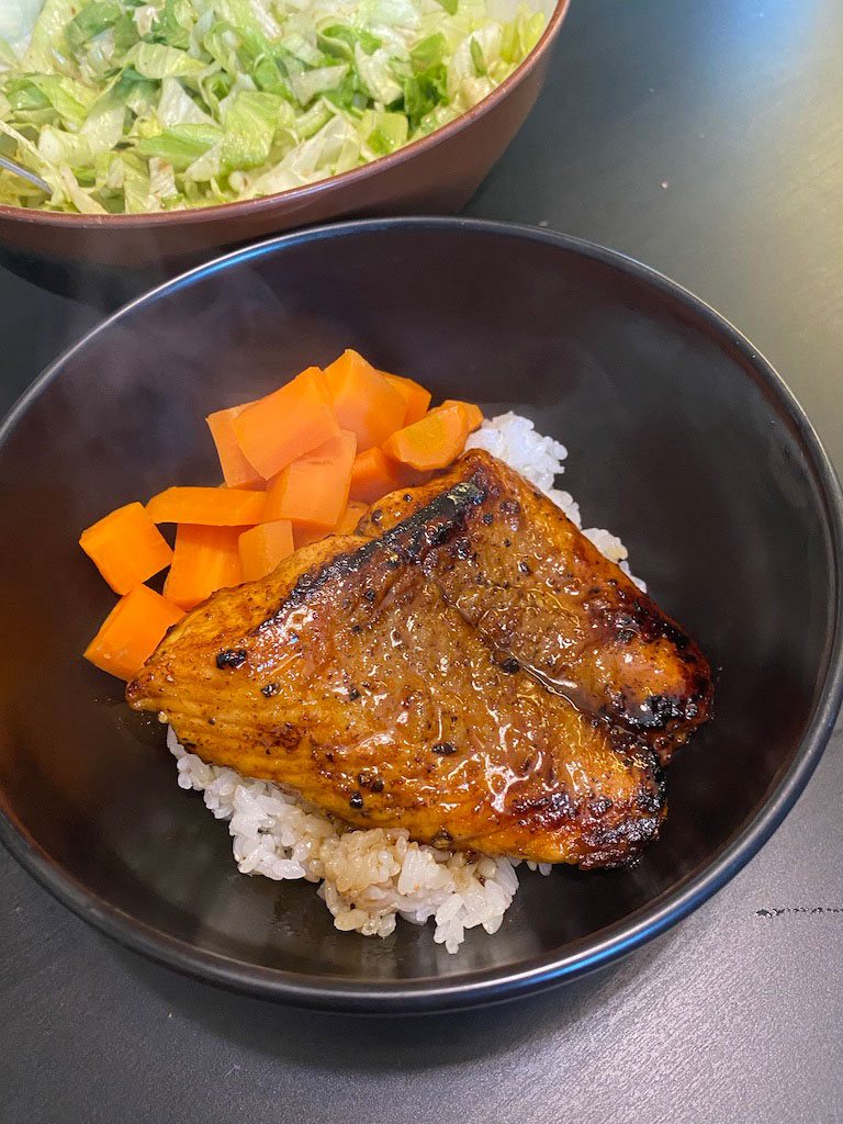 Teriyaki salmon on rice with carrots in a black bowl